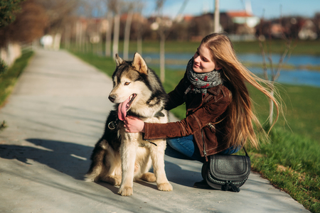 A girl is walking with a dog along the embankment. Beautiful Husky dog. The river. Spring.の写真素材