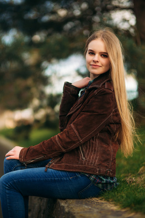 A beautiful girl is walking along the embankment. Blond hair and brown jacket. Spring.の写真素材