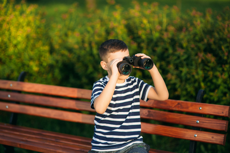 Little boy in a striped t-shirt looks through binoculars .Spring, sunny weather.の写真素材