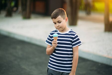 A little boy in a striped T-shirt is eating blue ice cream.Spring, sunny weather.の写真素材
