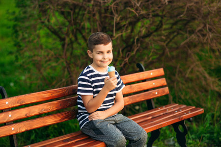 A little boy in a striped T-shirt is eating blue ice cream.Spring, sunny weather.