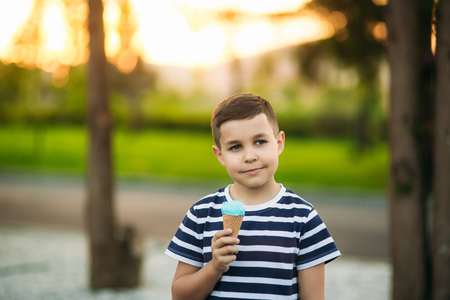 A little boy in a striped T-shirt is eating blue ice cream.Spring, sunny weather.の写真素材