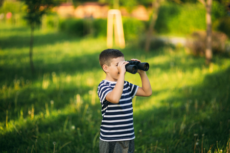 Little boy in a striped t-shirt looks through binoculars .Spring, sunny weather.の写真素材