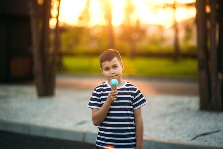 A little boy in a striped T-shirt is eating blue ice cream.Spring, sunny weather.の写真素材