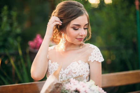 Young girl in wedding dress in park posing for photographer. Sunny weather, summer.