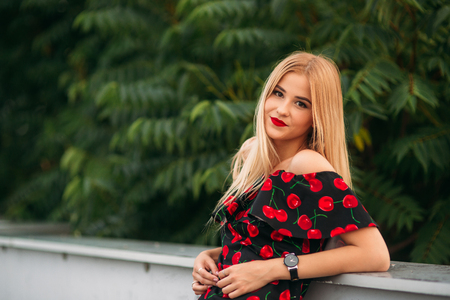 Beautiful girl posing for the photographer. Wearing in black and red dress. Smile, sunny day, summer.の写真素材
