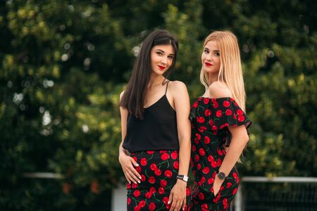 Beautiful girls posing for the photographer. Two sisters in black and red dress. Smile, sunny day, summer.の写真素材
