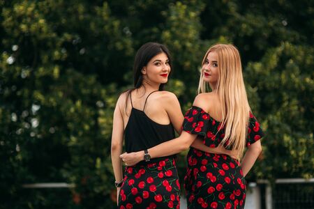 Beautiful girls posing for the photographer. Two sisters in black and red dress. Smile, sunny day, summer.の写真素材