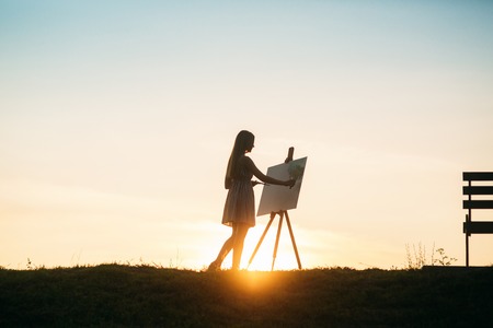 Silhouette of blonde girl paints a painting on the canvas.Palette with paints and spatula, summer sunny dayの写真素材