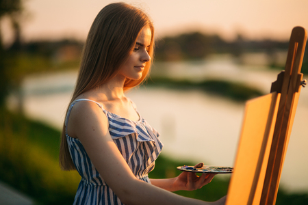 Silhouette of blonde girl paints a painting on the canvas.Palette with paints and spatula, summer sunny dayの写真素材