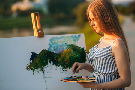 Silhouette of blonde girl paints a painting on the canvas.Palette with paints and spatula, summer sunny dayの写真素材