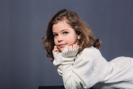 Little beautiful girl with brown hair in a light sweater and a skirt of tulle. Studio. A princess poses for a photographer.の写真素材