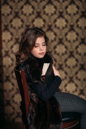 Beautiful little girl is reading a book in the library.の写真素材