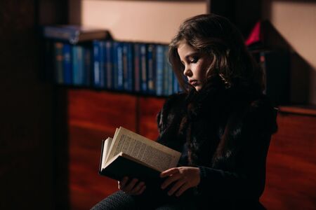 Beautiful little girl is reading a book in the library.の写真素材