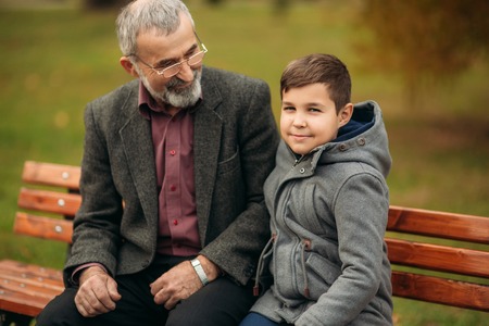Grandpa and his grandson spend time together in the park. They are sitting on the bench. Walking in the park and rejoicingの写真素材