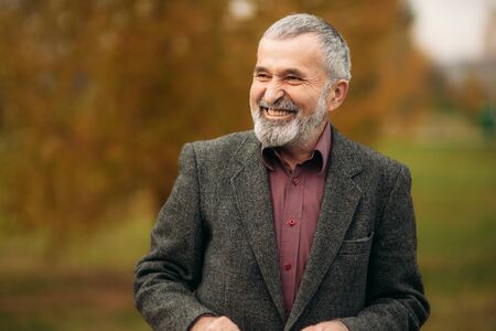 A handsome elderly man wearing glasses is using a phone. Walk in the park in autumnの写真素材