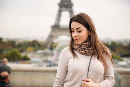 Beautiful girl posing to the photographer against the background of the Eiffel Tower. Autumn photosession. Sunny weather. Beautiful smile and makeupの写真素材