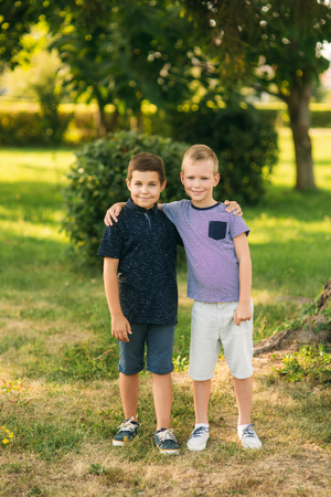 Two children are playing in the park. Two beautiful boys in T-shirts and shorts have fun smiling. They eat ice cream, jump, run. Summer is sunnyの写真素材