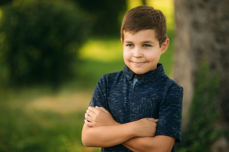 Handsome boy smiling and posing to the photographer. Joyful child walks the park. Sunny weather summerの写真素材