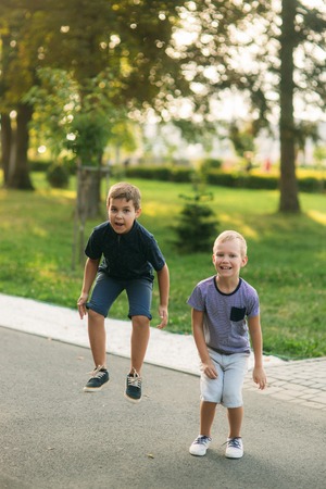 Two children are playing in the park. Two beautiful boys in T-shirts and shorts have fun smiling. They eat ice cream, jump, run. Summer is sunnyの写真素材