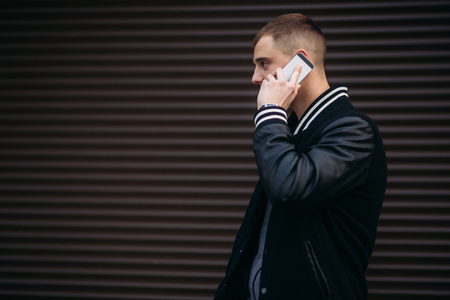 A young guy in a black jacket against a background of dark striped walls uses the phoneの写真素材