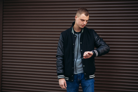 A young guy in a black jacket against a background of dark striped walls posing and smiling at the photographerの写真素材