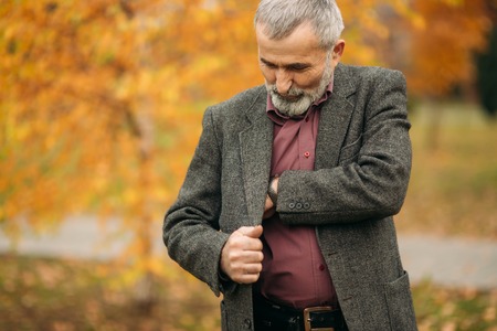 A handsome elderly man wearing glasses is using a phone. Walk in the park in autumnの写真素材