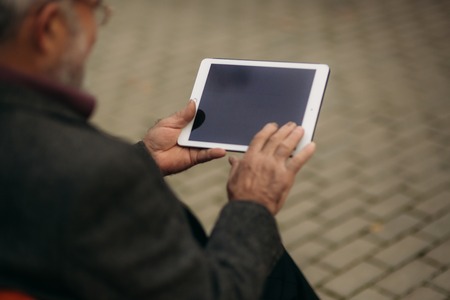 Grandpa use a tablet sitting in the pakr on the benchの写真素材