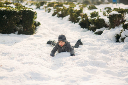 A boy in winter clothes jumps into the snow.