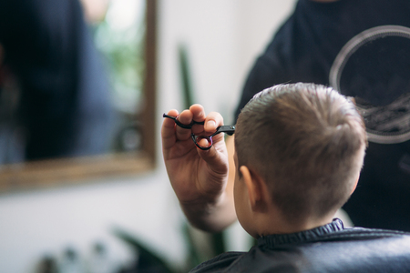 The boy getting haircut by scissor in barbershop. Barber use scissorの写真素材