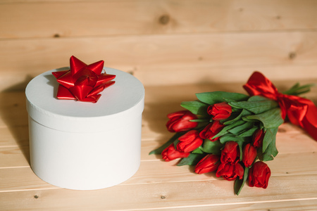 Beautiful red tulips with a gift. Red bow on a gift on a wooden backgroundの写真素材