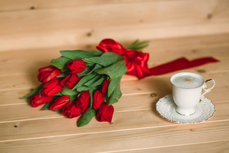 Beautiful red tulips and with a delicious cappuccino on a wooden backgroundの写真素材
