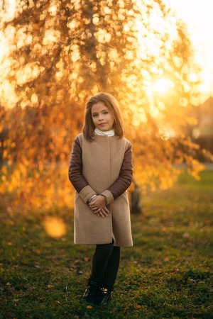 Little girl in autumn coat posing for photographer. Golden autumnの写真素材