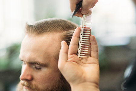 Barber using scissors and comb in barbershopの写真素材