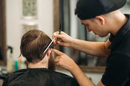 Master cuts hair and beard of men in the barbershop, hairdresser makes hairstyle for a young manの写真素材