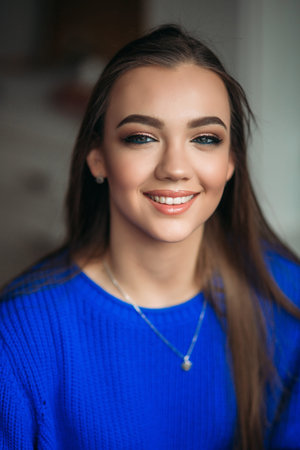 Beautiful brunette girl with a lovely smile in a blue blouse posing for a photographer and showing...