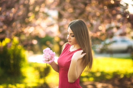 Beautiful girl posing to the photographer against the background of blooming pink trees. Spring. Sakuraの写真素材