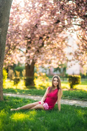 Beautiful girl posing to the photographer against the background of blooming pink trees. Spring. Sakuraの写真素材
