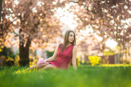 Beautiful girl posing to the photographer against the background of blooming pink trees. Spring. Sakuraの写真素材