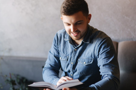 Handsome man with a beard reading a book in a cafe