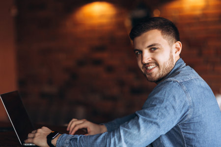 Man with a beard uses a laptop in a cafe