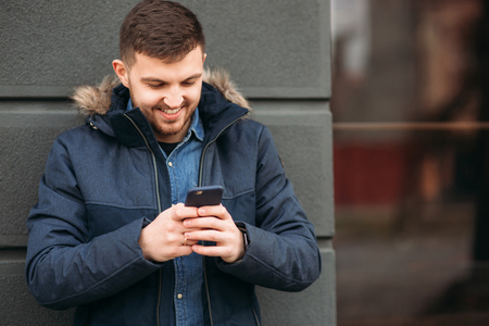 Handsome man in a jacket uses a phone standing on the streetの写真素材
