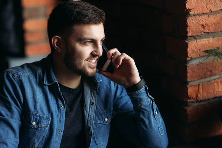 Bearded man in a denim shirt using phone inside a restaurantの写真素材