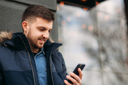Handsome man in a jacket uses a phone standing on the streetの写真素材