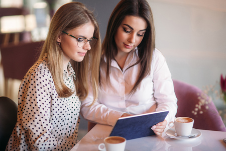 Two girls use a tablet while sitting in a cafe and drinking coffeeの写真素材