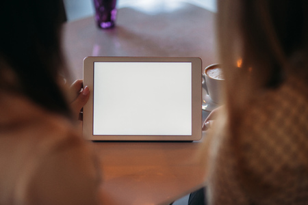 Two girls use a tablet while sitting in a cafe and drinking coffeeの写真素材