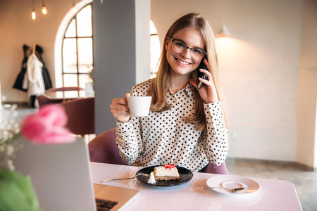 Girl eating cake in a cafe. Blonde in polka-dot shirt with laptopの写真素材