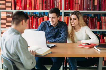 University students sitting together at table with books and laptop. Happy young people doing group...