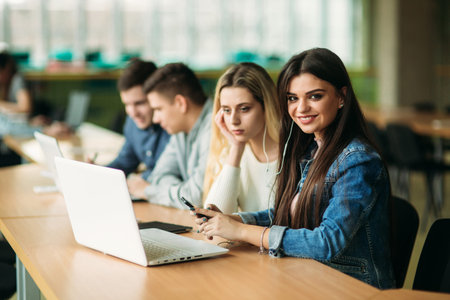 Group of college students studying in the school library, a girl and a boy are using a laptop and...