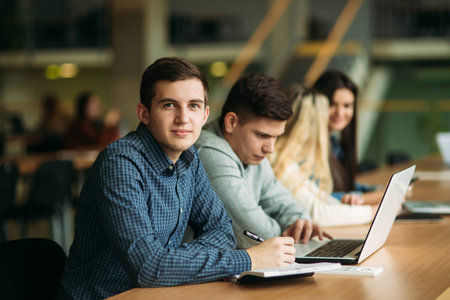 Group of college students studying in the school library, a girl and a boy are using a laptop and...